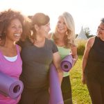Group Of Mature Female Friends On Outdoor Yoga Retreat Walking Along Path Through Campsite